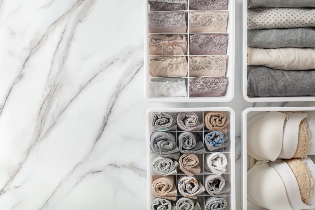 Womans underwear, pajamas and socks neatly folded and placed in closet organizer drawer divider on white marble table